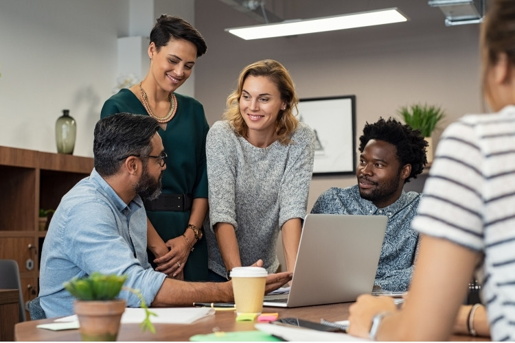 Equipe de trabalho reunida ao redor da mesa, sorrindo.