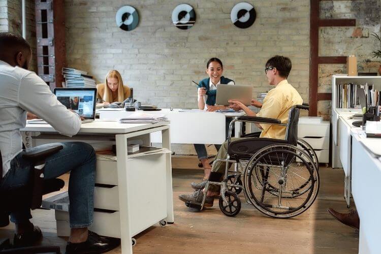 Cadeirante, homem negro e mulher convivendo em um ambiente de trabalho agradável.