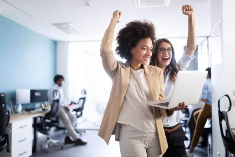 Mulheres de negócios com as mãos para cima, sorrindo e comemorando.