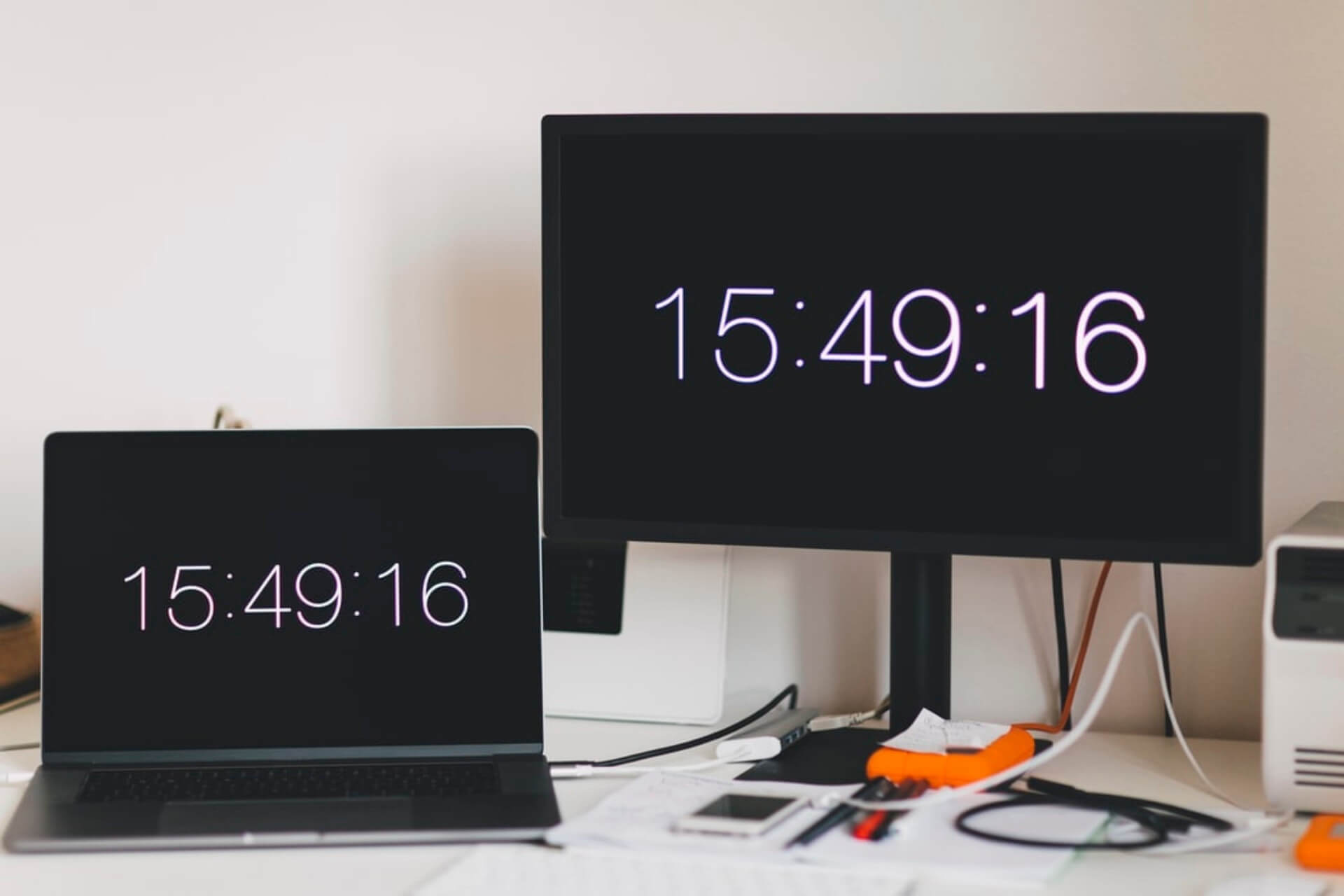 Notebook e monitor, um ao lado do outro, mostrando a hora.