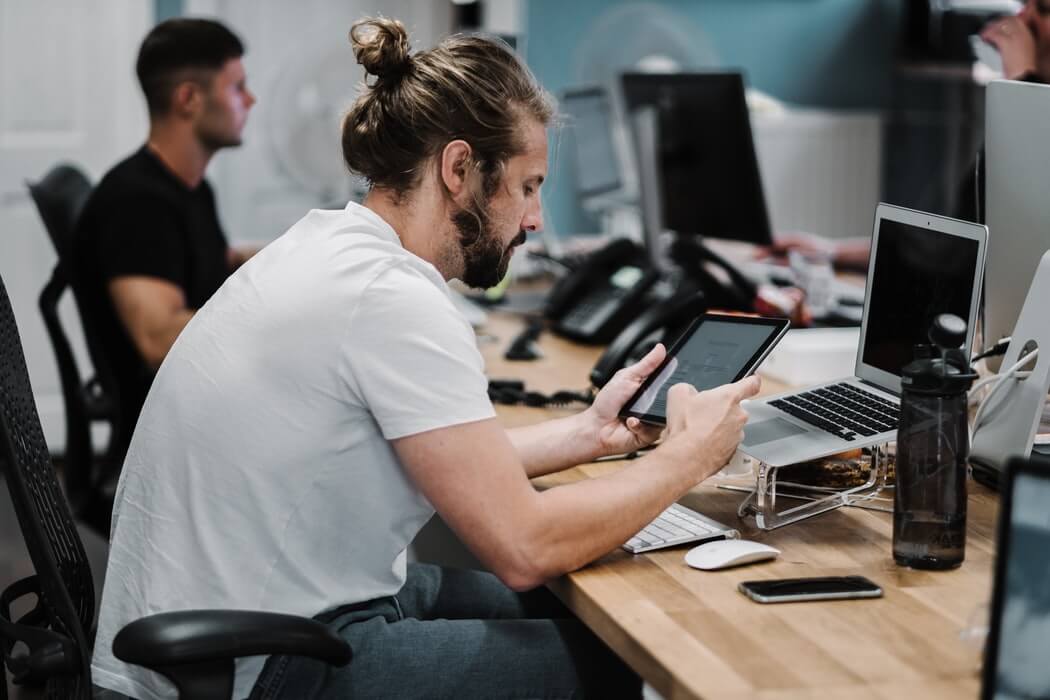 Homem sentado à mesa de trabalho, mexendo em um tablet.